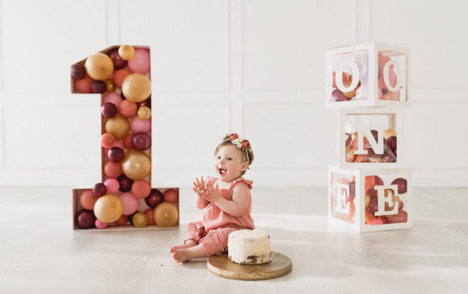 a baby sitting in front of a number and a cake. Event Photography By Bushel + Peck Photo