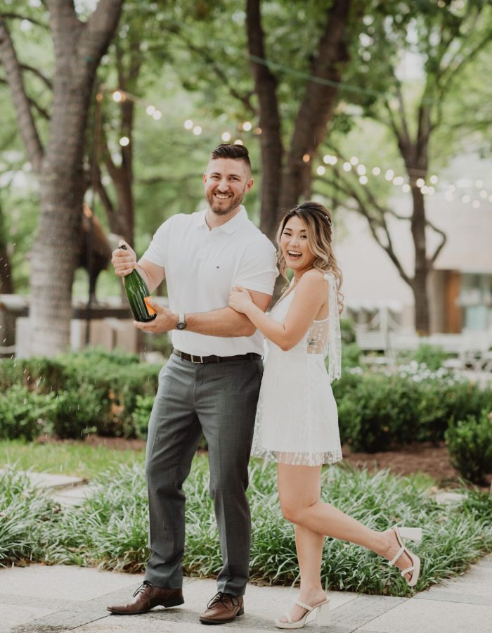 a man and woman standing in front of trees and a bottle of champagne. Photography Services By Bushel + Peck Photo